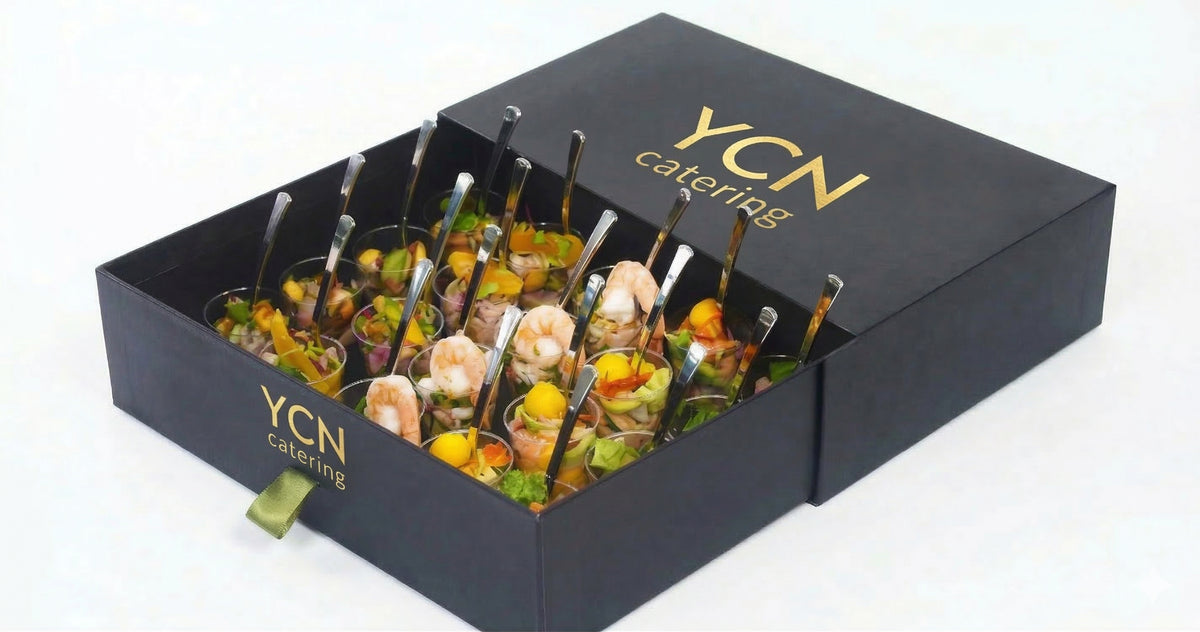 A black YCN Catering gift box containing multiple small skewered appetizers, photographed on a clean white background.