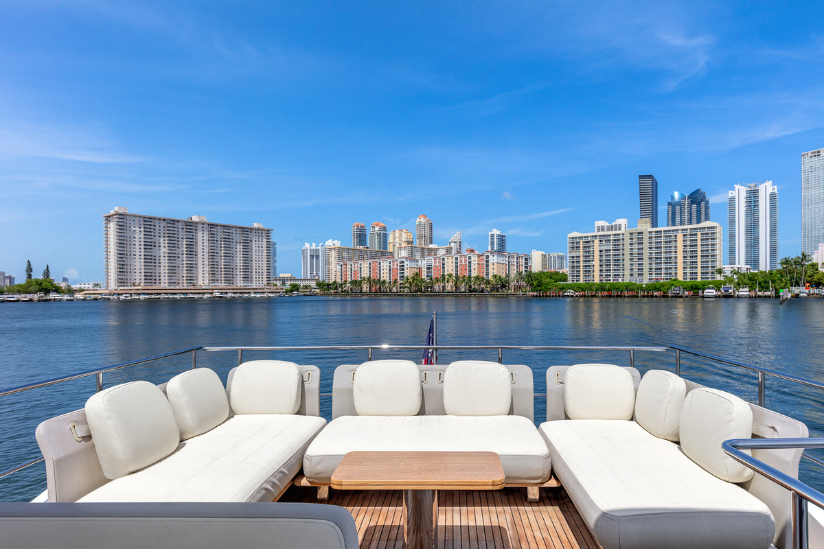 Flybridge lounge on Le Grand Bleu, with wraparound white seating, a teak table and skyline views
