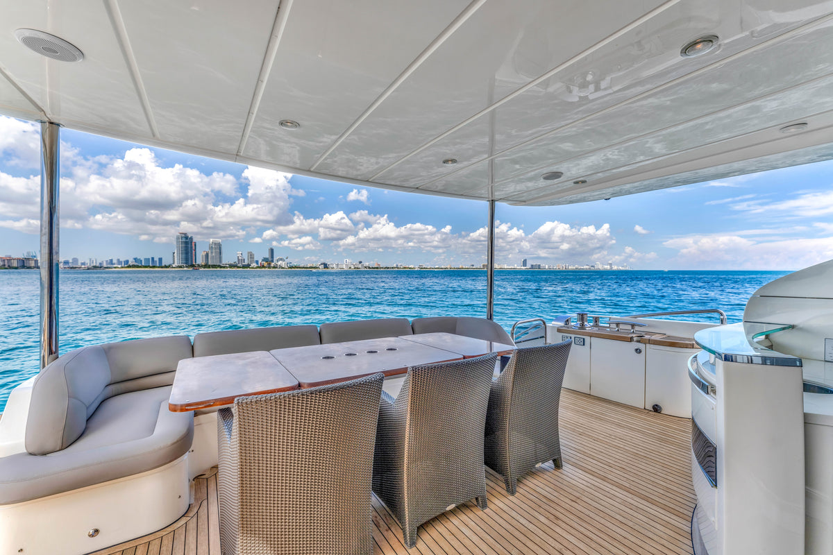 Shaded aft deck dining table and curved sofa aboard PRAYING FOR OVERTIME, looking out at the Miami skyline