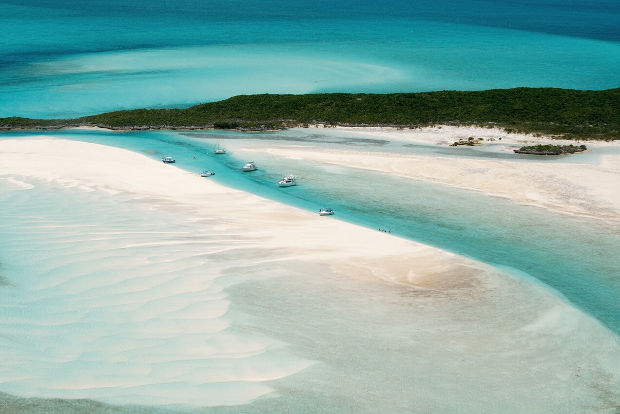 Boats anchored in a turquoise channel between white sandbars at Pipe Cay in the Exumas, Bahamas.